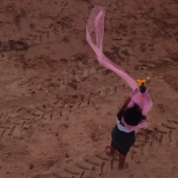 woman standing on a beach waving pink fabric in the wind