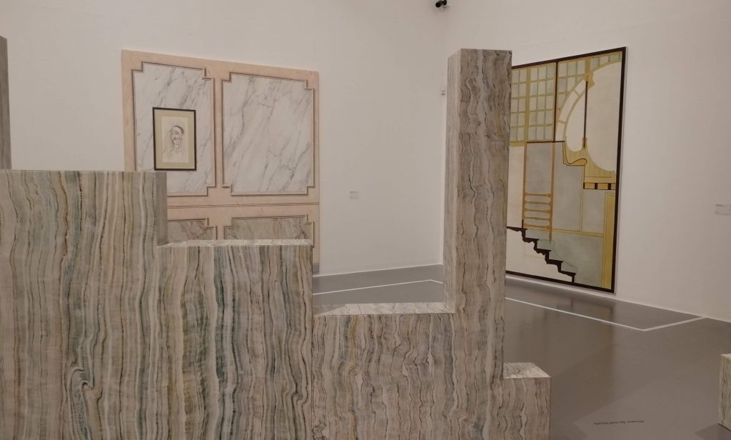 Installation shot from Lucy McKenzie exhibition at Tate. Looks over a marbleized wall towards two paintings,, one of which is a trompe l'oeil work showing marble panels and the other is an impression of a doorway and steps