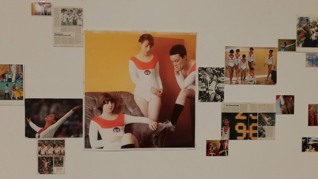 Installation show from Lucy McKenzie exhibition of "Top of the Will". Central large photos shows artist and her friends dressed as 1980s Soviet gymnasts with chosts of the actual gymnasts from magazines etc stuck to wall all around